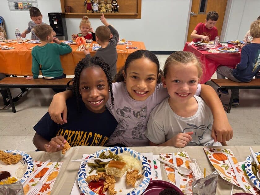 Elementary students smiling together at a Thanksgiving lunch in the cafeteria