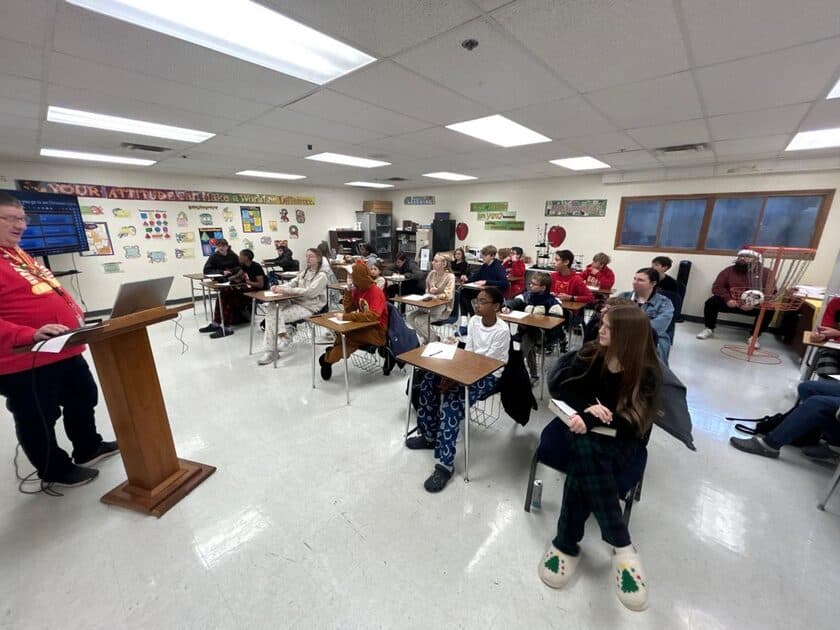 A high school class listens to a teacher lecture from the front of the classroom
