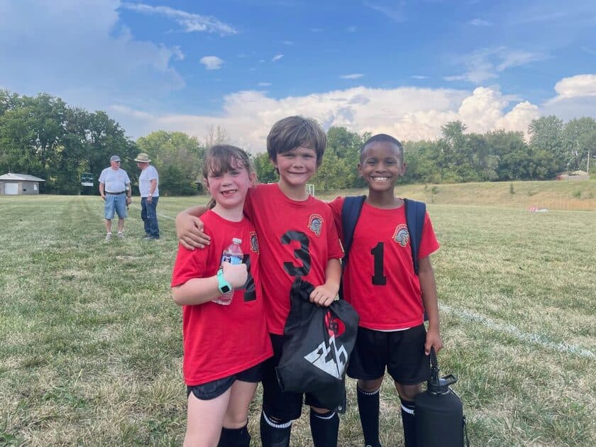 Three young soccer players in matching jerseys smile together after a game