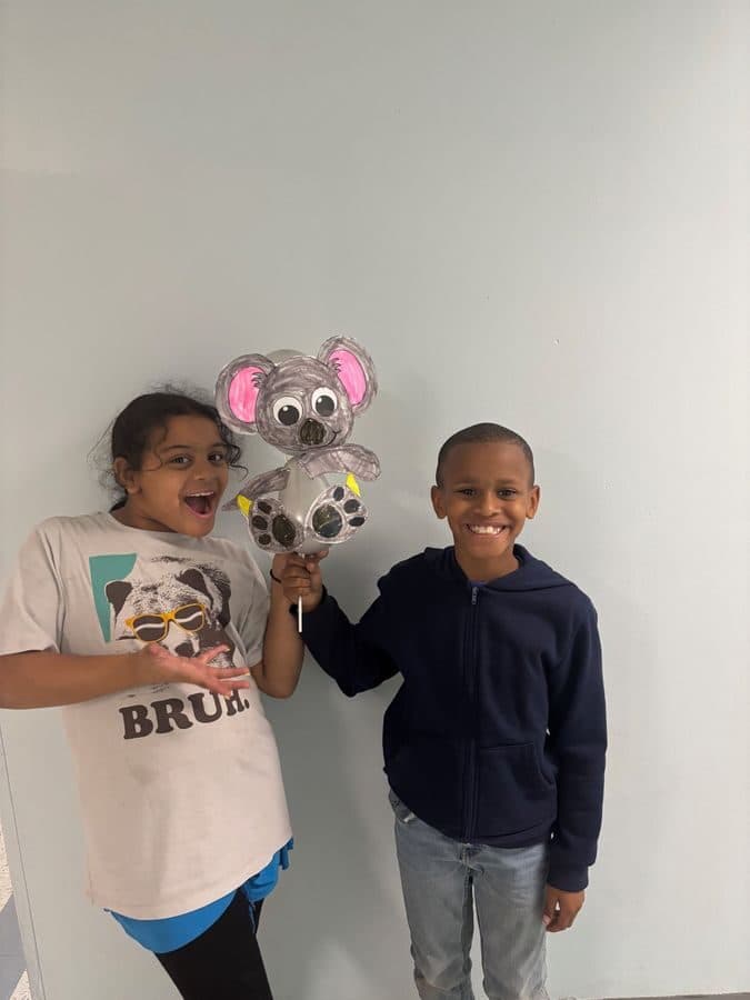 Two students show off a hand-painted koala craft they made together